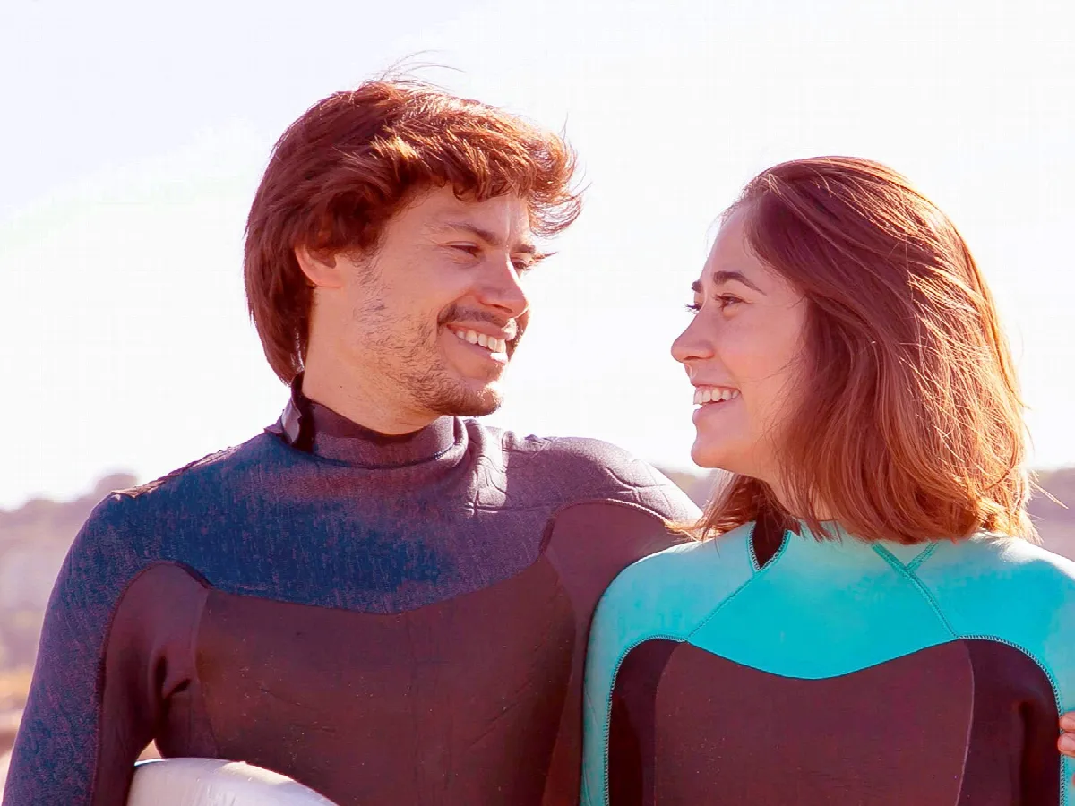 A smiling couple in wetsuits at the beach.